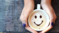 Smiley face on cappuccino foam, woman hands holding one cappuccino cup on wooden table