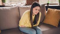 Photo of charming teen girl sit sofa suffer stomach pain wear yellow clothes modern interior flat indoors