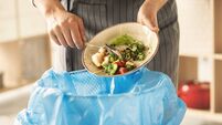 Woman scraping leftover food from plate into trash bin in kitchen