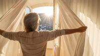 Man opening curtains in room at sunrise, idyllic sunlight