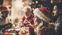 Happy woman with Santa's drinking wine during Christmas lunch at dining table.