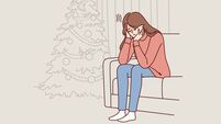 Woman is sitting on sofa near christmas tree and is sad because of loneliness and lack of friends
