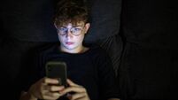 Teenage boy sitting on sofa using smart phone at night