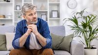 Adult mature man pensive sitting alone at home on sofa close up, gray haired person thinks looks towards window, depressed sad