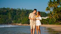 Romantic couple on beach holiday stroll hand in hand, sipping fresh coconuts. Laughing, chatting, they enjoy golden sunset. Perf