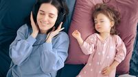Mother Wearing Headphones Listening a Podcast While Baby Sleeps