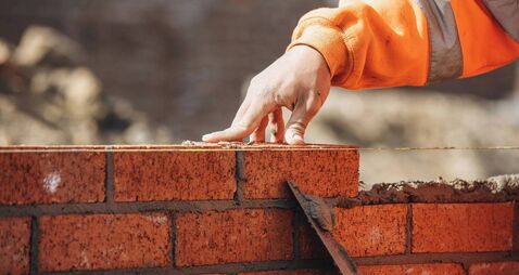 Bricklayer laying another brick in the wall on construction site for sturdy wall