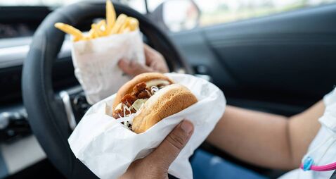 Asian lady holding hamburger and French fries to eat in car, dangerous and risk an accident.