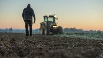 Male farmer with short brown hair,walking in the direction to his tractor,standing next to his agricultural field in the evening