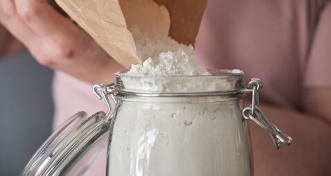 Unrecognizable latin man filling up a jar with wheat flour from a paper bag.