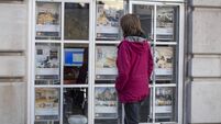 Woman looking at houses and flats in the window of an estate agent in London, UK